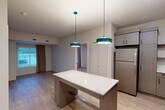 Located at 1550 Perimeter Pkwy NW in Huntsville, Alabama, this well-appointed 2-bedroom, 1-bathroom unit delivers a thoughtfully designed single-floor layout with modern finishes throughout. The open-concept kitchen and living area serves as the heart of the unit, featuring a central island with a clean white countertop illuminated by distinctive teal pendant lights. The kitchen is fully equipped with stainless steel appliances — including a refrigerator, range, dishwasher, and microwave — paired with taupe wood-grain cabinetry, white quartz countertops, and an undermount sink. Light wood-style luxury vinyl flooring flows seamlessly throughout the entire unit, lending a warm, cohesive aesthetic. Both bedrooms are bright and comfortable, each featuring large windows with floor-length drapes that invite natural light and outdoor views. Each bedroom includes its own dedicated closet, with the primary bedroom offering built-in shelving for added storage versatility. The shared bathroom is tastefully finished with a wide vanity, wood-toned cabinetry with black hardware, a backlit mirror, and a tub-shower combination. Additional conveniences include an in-unit laundry area and two closets, rounding out a practical and polished living space.