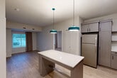 Located at 1550 Perimeter Pkwy NW in Huntsville, Alabama, this well-appointed 2-bedroom, 1-bathroom unit delivers a thoughtfully designed single-floor layout with modern finishes throughout. The open-concept kitchen and living area serves as the heart of the unit, featuring a central island with a clean white countertop illuminated by distinctive teal pendant lights. The kitchen is fully equipped with stainless steel appliances — including a refrigerator, range, dishwasher, and microwave — paired with taupe wood-grain cabinetry, white quartz countertops, and an undermount sink. Light wood-style luxury vinyl flooring flows seamlessly throughout the entire unit, lending a warm, cohesive aesthetic. Both bedrooms are bright and comfortable, each featuring large windows with floor-length drapes that invite natural light and outdoor views. Each bedroom includes its own dedicated closet, with the primary bedroom offering built-in shelving for added storage versatility. The shared bathroom is tastefully finished with a wide vanity, wood-toned cabinetry with black hardware, a backlit mirror, and a tub-shower combination. Additional conveniences include an in-unit laundry area and two closets, rounding out a practical and polished living space.
