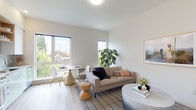 Located at 310 SE 12th Ave in Portland, Oregon, this single-floor unit offers a well-designed layout with a cohesive modern aesthetic. The open-concept living and dining area serves as the heart of the space, featuring light wood flooring, neutral white walls, and multiple windows that invite abundant natural light. Views of the surrounding neighborhood, including a glimpse of a historic red-brick church, add character to the setting. The living area accommodates both a dining nook and a comfortable lounge space, making it functional and versatile.

The kitchen is outfitted with white flat-front cabinetry, light quartz countertops, a subtle tile backsplash, stainless steel appliances including an electric range and over-the-range microwave, and an undermount sink — a clean, efficient design suited for everyday use.

The bedroom is a calm, understated retreat with warm-toned walls, light wood flooring, and ample room for a full-sized bed and furnishings. The bathroom features wood-look flooring, white tile wainscoting, a white vanity with integrated sink, and a large mirror, maintaining the unit's consistent modern and minimal design language throughout.