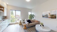 Located at 310 SE 12th Ave in Portland, Oregon, this single-floor unit offers a well-designed layout with a cohesive modern aesthetic. The open-concept living and dining area serves as the heart of the space, featuring light wood flooring, neutral white walls, and multiple windows that invite abundant natural light. Views of the surrounding neighborhood, including a glimpse of a historic red-brick church, add character to the setting. The living area accommodates both a dining nook and a comfortable lounge space, making it functional and versatile.

The kitchen is outfitted with white flat-front cabinetry, light quartz countertops, a subtle tile backsplash, stainless steel appliances including an electric range and over-the-range microwave, and an undermount sink — a clean, efficient design suited for everyday use.

The bedroom is a calm, understated retreat with warm-toned walls, light wood flooring, and ample room for a full-sized bed and furnishings. The bathroom features wood-look flooring, white tile wainscoting, a white vanity with integrated sink, and a large mirror, maintaining the unit's consistent modern and minimal design language throughout.