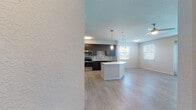 This well-designed single-floor residence offers a contemporary open-concept layout that seamlessly connects the kitchen, dining, and living areas. The kitchen is a standout feature, showcasing dark espresso cabinetry that reaches the ceiling, a mosaic tile backsplash, stainless steel appliances including a refrigerator, range, microwave, and dishwasher, and a crisp white countertop island with pendant lighting overhead. Light wood-style flooring runs throughout the main living areas, complementing the neutral color palette and creating a cohesive, modern aesthetic. The living area is bright and open, benefiting from multiple windows and a ceiling fan, with glass panel doors that invite an abundance of natural light. Bedrooms are generously sized with ceiling fans and large windows fitted with blinds. A notable feature is the spacious walk-in closet with built-in shelving, offering excellent storage capacity. The primary bathroom includes a glass-enclosed shower, dark vanity with white countertop, and tile flooring, while the secondary bathroom offers a full tub-shower combo and matching vanity finishes. Textured walls and ceilings add subtle architectural character throughout the space, rounding out this clean and functional modern residence.