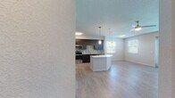 This well-designed single-floor residence offers a contemporary open-concept layout that seamlessly connects the kitchen, dining, and living areas. The kitchen is a standout feature, showcasing dark espresso cabinetry that reaches the ceiling, a mosaic tile backsplash, stainless steel appliances including a refrigerator, range, microwave, and dishwasher, and a crisp white countertop island with pendant lighting overhead. Light wood-style flooring runs throughout the main living areas, complementing the neutral color palette and creating a cohesive, modern aesthetic. The living area is bright and open, benefiting from multiple windows and a ceiling fan, with glass panel doors that invite an abundance of natural light. Bedrooms are generously sized with ceiling fans and large windows fitted with blinds. A notable feature is the spacious walk-in closet with built-in shelving, offering excellent storage capacity. The primary bathroom includes a glass-enclosed shower, dark vanity with white countertop, and tile flooring, while the secondary bathroom offers a full tub-shower combo and matching vanity finishes. Textured walls and ceilings add subtle architectural character throughout the space, rounding out this clean and functional modern residence.
