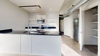 Located at 310 E 1st St in Tulsa, Oklahoma, this one-bedroom, one-bathroom unit offers a well-designed layout with a distinct industrial-modern aesthetic. Polished concrete floors extend throughout the entire space, complementing the clean lines and neutral gray palette found in every room.

The kitchen is a standout feature, anchored by a central island with a dark granite countertop and an integrated sink with a flexible faucet. White shaker-style cabinetry lines the walls alongside open floating shelves, and stainless steel appliances — including a range, microwave, and refrigerator — complete the contemporary look. An exposed metallic ventilation duct runs overhead, adding to the space's industrial character.

The bedroom is a comfortably proportioned room featuring a ceiling fan with light fixture and crisp white trim. The room connects to a dedicated closet and is accessible via a hallway that provides a natural separation between living and sleeping areas.

The bathroom includes a glass-enclosed walk-in shower with clean tile surround and chrome hardware. An exposed concrete column adds a raw, urban architectural detail to the space.

Throughout the unit, recessed lighting, visible HVAC infrastructure, and consistent use of white and gray tones create a cohesive, modern loft-style atmosphere well-suited to urban living in Tulsa's vibrant East Village neighborhood.