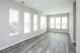 This single-floor residence presents a thoughtfully designed layout with a cohesive contemporary aesthetic throughout. The open-concept kitchen and living area serves as the heart of the space, where wood-look plank flooring extends across the common areas, complementing the warm, neutral palette of the walls. A row of large windows floods the living area with abundant natural light and provides views of the surrounding neighborhood.

The kitchen is well-appointed with dark walnut-toned cabinetry, stainless steel appliances including a refrigerator, electric range, and over-the-range microwave, and a light quartz peninsula countertop with an integrated sink. Pendant lighting accents the peninsula, adding a refined touch.

The bedrooms are comfortably sized and carpeted in a neutral tone, each featuring windows that allow natural light and outdoor views. The two bathrooms maintain a consistent modern design, featuring dark wood-grain vanities with white quartz countertops, undermount sinks, chrome fixtures, and wood-look tile flooring. One bathroom includes a wall-mounted mirror with overhead lighting. The overall design is clean, modern, and functional, with a consistent material palette unifying the entire space.