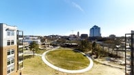 Located on Foster Street in Durham, North Carolina, this outdoor space offers a well-maintained green lawn as its centerpiece, encircled by a smooth, paved walking path that invites leisurely strolls and light recreation. The circular layout creates a defined yet open gathering area, framed by mature trees that line the perimeter and provide natural character to the landscape. The level terrain makes the space accessible and versatile for a variety of uses.

From this elevated vantage point, the space commands impressive panoramic views of downtown Durham's skyline, including recognizable high-rise buildings and active development marked by construction cranes, reflecting the city's ongoing growth. The surrounding area features additional open land, pathways, and scattered tree cover, contributing to a park-like atmosphere. To the west, urban infrastructure and neighboring structures are visible, reinforcing the space's convenient proximity to the heart of the city.

Under open skies with abundant natural light, the grounds feel expansive and inviting. The combination of green space, a defined circular path, and striking downtown views makes this an appealing outdoor destination in the Durham urban landscape.