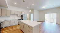 This well-appointed 2-bedroom, 2-bathroom residence offers a thoughtfully designed single-floor layout with a clean, contemporary aesthetic throughout. The open-concept kitchen and living area serves as the heart of the home, anchored by a central island with a white quartz countertop and pendant lighting above. The kitchen is outfitted with flat-front cabinetry in a warm gray-white finish, stainless steel appliances including a refrigerator, range, microwave, and dishwasher, and a undermount sink. Light hardwood flooring flows throughout the main living areas, lending warmth and continuity to the space. Sliding glass doors in the living area invite natural light and provide access to an outdoor balcony with mountain views. Both bedrooms feature neutral carpet, windows with views of the surrounding landscape, and dedicated closets with built-in wire shelving. The primary bathroom offers a double-sink vanity with a long mirror, modern fixtures, and hardwood-style flooring. The second bathroom includes a tiled tub-shower combination and hardwood-style flooring. Two closets provide ample storage throughout the residence, completing this functional and modern home.