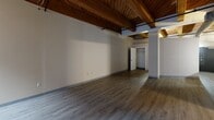 Located on the historic Washington Avenue corridor in downtown St. Louis, this 2-bedroom, 1-bathroom loft blends industrial character with modern comfort. The space is defined by its striking exposed wood beam ceilings with tongue-and-groove planking, original brick accent walls, and durable wood-look plank flooring that runs throughout. Oversized windows flood the living area with natural light while offering views of the surrounding urban streetscape.

The open-plan kitchen and dining area features light maple cabinetry, granite-look countertops, stainless steel appliances including a dishwasher and range, and a peninsula breakfast bar — all set beneath pendant lighting and those signature timber beams. Exposed ductwork reinforces the loft's industrial aesthetic.

The generously sized primary bedroom includes closet access and maintains the same warm ceiling treatment, creating a cohesive feel. The second bedroom offers similar proportions with its own closet. The bathroom is clean and functional, appointed with white subway tile surrounding a full soaking tub and shower combination, complemented by matte black fixtures and hardware. Two additional closets provide ample storage throughout the unit. The overall ambiance is urban and characterful, ideal for those who appreciate architectural history paired with updated living spaces.
