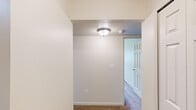 This single-floor unit offers a practical and efficiently designed layout, incorporating a living room, kitchen, bedroom, bathroom, and two hallways. Neutral-toned walls and carpet flooring throughout the main areas create a clean, understated aesthetic that provides a versatile canvas for furnishing.

The galley-style kitchen is equipped with warm medium-toned wood cabinetry on both sides, light-colored countertops, a stainless steel sink, and white appliances including an electric range and refrigerator. Tile flooring runs through the kitchen, which connects directly to a hallway with additional closet storage.

The bedroom features soft carpet flooring, a window with vertical blinds offering views of surrounding greenery, and a built-in closet with bifold doors and a shelf rod — providing practical storage within a well-proportioned space.

The hallways are finished with carpet and flush-mount ceiling lighting, providing clear circulation between rooms. A smoke detector is also present, noting attention to safety.

The bathroom includes a single-sink vanity with warm wood cabinetry, a mirrored medicine cabinet, tile flooring, and a full tub/shower combination with white tile surround and a chrome curtain rod.