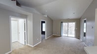 This 2-bedroom, 1-bathroom single-floor residence offers a well-organized layout designed for comfortable everyday living. The main living area is a standout feature, showcasing vaulted ceilings that lend a sense of openness and volume to the space. Neutral gray walls and wall-to-wall carpeting in a warm beige tone create a clean, understated aesthetic throughout. Large sliding glass doors in the living area flood the space with natural light and provide direct access to a balcony overlooking a wooded outdoor setting, offering a tranquil natural backdrop. White trim and door frames provide crisp contrast against the soft gray walls, contributing to a tidy, cohesive look. The open flow between the living area and the adjoining rooms supports an easy, functional traffic pattern. The two bedrooms are accessible from the main living space and benefit from the same neutral palette and carpeted flooring. The single bathroom completes the layout, keeping the floor plan efficient and straightforward. Overall, this residence delivers a bright, calm atmosphere with architectural interest provided by the vaulted ceiling, making it a practical and inviting single-floor home.