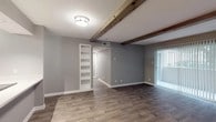 This well-appointed single-floor residence blends modern updates with charming character details throughout. The main living area immediately draws attention with its striking exposed wood ceiling beams, which add a warm, rustic contrast to the contemporary gray-toned walls and rich wood-look flooring that extends seamlessly throughout the space. Built-in wall shelving provides convenient storage and display space, while a large sliding glass door fitted with vertical blinds allows natural light to pour in. A central hallway connects the living area to the rest of the home, maintaining a logical and comfortable flow.

The kitchen has been thoughtfully renovated and features crisp white shaker-style cabinetry, light quartz countertops, a stainless steel double-basin sink, and a full suite of stainless steel appliances including a range, microwave, and dishwasher. A window above the counter brings in additional natural light.

The bedrooms continue the cohesive design aesthetic with matching wood-look flooring, gray walls, ceiling fans, and sliding glass doors that offer access to natural light and outdoor views. The bathroom is finished with a white quartz vanity and a tub-shower combination elegantly surrounded by large-format marble-look tile, delivering a clean and polished look throughout.
