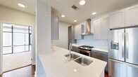 This thoughtfully designed 2-bedroom, 2-bathroom residence offers a cohesive modern aesthetic throughout its single-floor layout. The kitchen serves as a standout centerpiece, featuring quartz countertops with a double stainless steel sink, gray shaker-style cabinetry, a subway tile backsplash, stainless steel appliances including a gas range and French door refrigerator, a professional-grade range hood, and a pendant light accent — all combining for a sleek, functional workspace. The living room is bathed in natural light through large windows framing urban cityscape views, and features warm hardwood-style flooring and a ceiling fan overhead. Both bedrooms are carpeted for comfort, each offering generous windows with city views and ceiling fans. The primary bedroom includes a dedicated closet with built-in shelving for organized storage. The two bathrooms are finished consistently with gray cabinetry, quartz countertops, and light tile flooring. One bathroom features a tub-shower combination with classic subway tile surround, while the other offers a single vanity with a large mirror. The space also includes two closets, providing practical storage solutions throughout. Clean neutral walls and recessed lighting tie the entire residence together with a polished, contemporary feel.