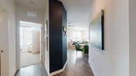 This single-floor residence combines contemporary design with vibrant, curated interiors throughout. The entryway sets the tone immediately, featuring a striking navy accent wall paired with rich hardwood-style flooring that extends throughout the main living areas. A large-scale abstract canvas greets guests along the hallway, leading seamlessly into the combined dining and living space.

The living room is bright and inviting, with generous windows dressed in sheer white curtains and plantation shutters that allow abundant natural light. A ceiling fan anchors the room, which flows naturally into the dining area furnished with emerald green chairs around a round table. The kitchen offers ample cabinetry in a warm greige finish, granite countertops, a classic white subway tile backsplash, and a full suite of stainless steel appliances.

Both bedrooms feature distinct accent walls — one in soft sky blue and one in deep navy — lending each room a defined character. The bathrooms maintain the same refined finishes seen throughout, with granite-topped vanities, dark cabinetry, and hardwood-style flooring. The overall ambiance of the residence is cohesive and polished, balancing bold color choices with clean architectural lines for an inviting, well-designed living environment.