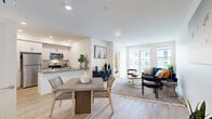 Located at 200 E 31st St in National City, CA, this single-floor residence offers two bedrooms and two bathrooms within a thoughtfully designed open-concept layout. The combined kitchen and living area serves as the heart of the home, featuring light wood-style flooring, recessed lighting, and large sliding glass doors that open to a private balcony overlooking a community courtyard and pool. The contemporary kitchen is equipped with stainless steel appliances — including a refrigerator, range, microwave, and dishwasher — complemented by sleek grey quartz countertops, a peninsula with a built-in sink, and crisp white cabinetry. The living area provides a bright, airy atmosphere with ample natural light. The primary bedroom includes an en-suite bathroom and a dedicated mini-split climate control unit, while the second bedroom features a large window that brings in natural light. Both bathrooms are finished in a clean, modern style with tiled tub-shower combinations, wood-look flooring, and white vanities. A hallway connects the living spaces to the bedrooms, with an additional closet for storage. The building exterior showcases a Spanish-inspired design with a tiled roof, teal shutters, and a landscaped courtyard with a pool.