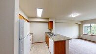 Located in Covington, WA, this two-bedroom, one-bathroom residence offers a practical and well-organized single-floor layout. The kitchen is a standout feature, equipped with warm-toned wood cabinetry, laminate countertops, a peninsula with a double-basin sink, a white electric range, and a full-size refrigerator. A skylight and recessed lighting keep the kitchen bright, while tile flooring adds durability underfoot. The kitchen flows naturally into the adjacent living area, which is finished with neutral carpet and maintains a clean, open feel. Both bedrooms are carpeted and feature windows overlooking lush, tree-lined surroundings, filling the rooms with natural light and peaceful greenery views. The primary bedroom includes a sliding-door closet, providing organized storage. Baseboard heaters in the bedrooms ensure efficient warmth. The bathroom is well-appointed with a single-sink vanity with wood cabinetry, a large mirror, tile flooring, and a bathtub. Neutral tones and warm wood accents run consistently throughout the residence, creating a cohesive and understated aesthetic. The wooded views visible from multiple rooms add a serene, natural backdrop to everyday living in this Covington community.