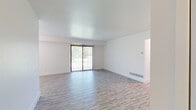 This single-floor residence is thoughtfully laid out to maximize functionality and natural light throughout. The spacious living room serves as the heart of the unit, featuring light-toned wood-style flooring, crisp white walls, and a large sliding glass door fitted with vertical blinds that opens to an outdoor view of lush greenery. A side window and a chandelier overhead further brighten the space, creating an airy and welcoming atmosphere.

The kitchen is outfitted with white shaker-style cabinetry, dark granite countertops, a classic subway tile backsplash, and stainless steel appliances including an electric range and over-the-range microwave. Wood-style flooring continues seamlessly through this area, complementing the clean, modern aesthetic.

The bedrooms are carpeted for added comfort and each feature windows with blinds that allow natural light to filter in. At least one bedroom includes a built-in closet with bifold doors, providing practical storage. An additional room with wood-style flooring offers flexible use as a bedroom or office.

The bathroom is finished in an all-white palette, featuring a single-sink vanity with white cabinetry, a large mirror, and a tub-shower combination, all set on wood-style flooring for a cohesive look.
