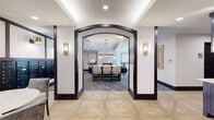 Located at 1408 Montgomery St in Savannah, Georgia, this single-floor amenity space combines refined design with practical function. The entry foyer is defined by dramatic dark-trimmed archways and geometric parquet wood flooring that establish a polished, upscale aesthetic throughout.

The mail and lounge area features a wall of built-in mailboxes framed by gold sconce lighting and curated artwork. A marble-topped round table with plush velvet chairs provides a comfortable spot to sort correspondence.

Adjacent to the mail area, a spacious lounge invites residents to relax on tufted navy and charcoal sofas arranged around a sleek, floor-to-ceiling marble fireplace. Circular wall-mounted sconces and layered area rugs add warmth and texture to the space.

A dedicated conference zone, accessible through the arched entryway, centers on a long wooden table with upholstered counter-height seating beneath a striking brass-and-crystal chandelier. Tray ceilings and large glass doors allow natural light to filter in, enhancing the room's airy, professional atmosphere.

The refreshment bar features bold navy cabinetry, a geometric hexagonal tile backsplash, a beverage refrigerator, and coffee station — offering a functional and visually distinctive amenity. Throughout, dark column accents and brass fixtures tie the design together cohesively.