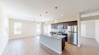 This single-floor residence offers a thoughtfully designed open-concept layout that seamlessly connects the kitchen, dining, and living areas. The kitchen serves as a central hub, showcasing dark espresso cabinetry, granite countertops, a large center island with a built-in sink, stainless steel appliances, and pendant lighting that adds a contemporary touch. Natural light filters in through multiple windows dressed with horizontal blinds, enhancing the warm, neutral palette found throughout the home.

Wood-look plank flooring runs through the main living spaces, providing both durability and aesthetic appeal. The spacious living area features a ceiling fan with light kit and a welcoming front entry with direct exterior window views. Bedrooms are fitted with ceiling fans, and flooring transitions to plush carpet, creating a comfortable atmosphere. One bedroom includes a walk-in closet with wire shelving systems for organized storage.

The bathroom is finished with dark cabinetry, granite countertops, wood-look flooring, and a full tub-shower combination with tile surround. Clean white walls and consistent neutral tones throughout lend the space a cohesive, move-in-ready character.