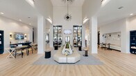Located at 1559 W Nine Mile Rd in Pensacola, Florida, this single-story community clubhouse delivers a sophisticated blend of modern design and practical amenities. The grand entrance lobby commands attention with soaring ceilings, white structural columns, and a dramatic starburst chandelier suspended above a curved, tufted lounge sofa centered on a soft area rug. Black-framed glass partition walls add a contemporary architectural element while allowing natural light to flow throughout.

The expansive open lounge area continues the elevated aesthetic with vaulted ceilings, light hardwood flooring, and an eclectic mix of seating arrangements — from navy sectionals to sculptural accent chairs — creating versatile spaces for socializing or relaxing. Adjacent, a fully appointed kitchen and dining area features Edison-style pendant lighting, white cabinetry with a textured tile backsplash, a coffee station, and a long communal table ideal for gatherings.

Black-framed glass-enclosed private rooms offer quieter settings for focused work or meetings. The fitness center is well-equipped with cardio machines, strength equipment, and ample natural light. A dedicated mailroom with bold navy and yellow cabinetry and warm pendant lighting adds a design-forward touch to everyday convenience. Throughout, the space maintains a cohesive, upscale ambiance with curated artwork and thoughtful furnishings.