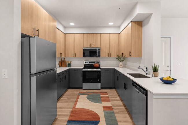 Staged kitchen showcasing the stainless steel appliance package, two-tone cabinetry, and ample workspace. - 27 West Apartments