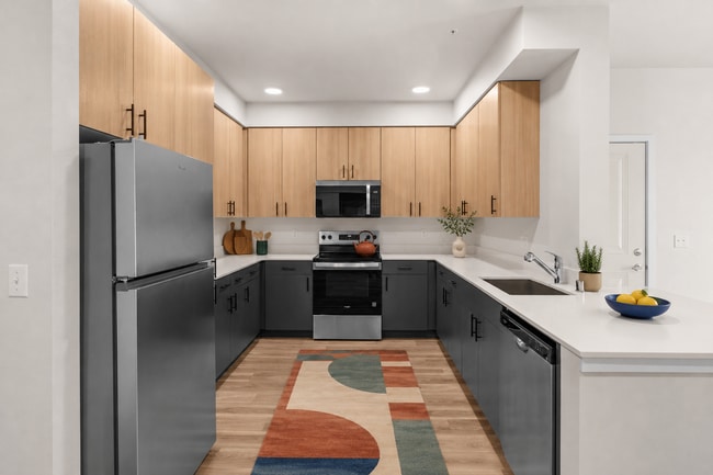 Staged kitchen showcasing the stainless steel appliance package, two-tone cabinetry, and ample workspace. - 27 West Apartments