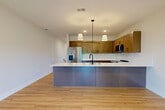 Located in Omaha, Nebraska, this well-appointed 1-bedroom, 1-bathroom two-story residence offers a thoughtfully designed layout spread across two levels. The main living floor showcases an open-concept kitchen and living room finished with warm light hardwood flooring throughout. The kitchen is a standout feature, equipped with stainless steel appliances including a refrigerator, gas range, and built-in microwave, complemented by rich wood shaker cabinetry with matte black hardware and crisp white countertops. A peninsula with an undermount sink and pendant lighting adds both function and style. The living area flows seamlessly to a private balcony through sliding glass doors, offering pleasant outdoor views of surrounding greenery. A tile-surround fireplace anchors the living space, adding warmth and character. The bedroom is carpeted for comfort, features a ceiling fan, and includes a large window for natural light, along with access to a dedicated closet. The full bathroom is finished with light hardwood-style flooring, a wood vanity with matte black fixtures, and a full tub-shower combination. A conveniently located in-unit laundry room with a top-load washer and dryer completes the home's practical offerings.