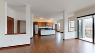 This single-floor residence offers a thoughtfully designed open-concept layout that seamlessly connects the kitchen and living area. The kitchen is a standout feature, showcasing rich warm-toned cabinetry, dark granite countertops, a central island, and a full suite of stainless steel appliances including a refrigerator, range, and built-in microwave. Track lighting illuminates the space, and large windows allow natural light to fill the open living area, which is finished with warm hardwood-style flooring throughout. The bedroom areas are carpeted for comfort and include generous closet storage, highlighted by a spacious walk-in closet fitted with wire shelving systems for organized storage. The bathroom is clean and functional, featuring tile flooring, a sliding glass enclosed shower stall, and warm wood-toned vanity cabinetry. A dedicated in-unit laundry room houses a full-size washer and dryer with an overhead shelf for additional storage. A utility room with HVAC equipment and pantry-style shelving provides further practical storage. White trim and neutral wall tones throughout the space create a bright, cohesive aesthetic.