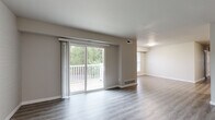 This single-floor residence offers a thoughtfully designed layout with modern updates and a clean, neutral palette throughout. The open living area is a standout feature, anchored by durable wood-look flooring and a large sliding glass door that floods the space with natural light and provides direct access to a private deck overlooking lush greenery. An accent wall with painted white brick adds texture and character to the living space.

The kitchen has been tastefully updated with two-tone cabinetry — white upper cabinets paired with dark lower cabinets — complemented by marble-style countertops, a white subway tile backsplash, stainless steel appliances, and a wall-mounted range hood. A dedicated dining area adjacent to the kitchen offers a natural flow for everyday living.

The bedrooms feature soft carpeting, generous closet space with built-in rods, and windows that bring in abundant natural light with views of surrounding trees. The bathroom is finished with light wood-look flooring, a tiled tub-and-shower combination featuring a decorative blue mosaic accent strip, and clean white fixtures.

Throughout the residence, consistent wood-look flooring, neutral gray walls, and bright white trim create a cohesive and modern atmosphere that is both functional and inviting.