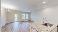 Located at 1004 Wildflower in Wilmington, NC, this two-story home offers a thoughtfully designed layout spread across two floors. The main level features an open-concept living, dining, and kitchen area bathed in natural light from multiple windows, with warm wood-look flooring flowing throughout. The kitchen is well-appointed with white shaker cabinetry, granite countertops, a breakfast bar with an undermount sink, subway tile backsplash, and stainless steel Whirlpool appliances. A ceiling fan anchors the living area, while a elegant chandelier adds a refined touch to the dining space. A pantry and a convenient half bath round out the first floor, along with an attached garage. Upstairs, the primary bedroom is generously sized and accompanied by a luxurious en-suite bathroom featuring a dual-sink vanity with white quartz countertops, light wood flooring, and a glass-enclosed walk-in shower with classic subway tile. Two additional bedrooms, each with closets and hardwood-style flooring, share access to well-appointed bathrooms. A dedicated laundry room with a full-size washer and dryer adds everyday convenience. The home's clean, neutral palette and modern finishes create a bright, welcoming atmosphere throughout.