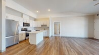 This single-floor unit offers a thoughtfully designed open-concept layout that seamlessly connects the kitchen and living areas. The kitchen is outfitted with crisp white shaker-style cabinetry, a central island with light countertops, and a full suite of stainless steel appliances including a refrigerator, range, microwave, and dishwasher. Warm-toned wood-look flooring runs throughout the main living areas, adding a cohesive and inviting feel. The spacious living room benefits from vaulted ceiling details, a ceiling fan, and sliding glass doors that open onto a private balcony, filling the room with natural light. The bedroom is generously sized and features plush carpeting for added comfort. Two full bathrooms serve the unit — one with a tub/shower combo, single vanity, and wood-look flooring, and a second elongated bathroom featuring a wide vanity with ample cabinetry and a large mirror. A dedicated in-unit laundry room provides added convenience, complete with a full-size washer and dryer and built-in shelving. Throughout the space, neutral wall tones, recessed lighting, and clean architectural lines create a bright, modern, and functional living environment.