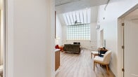Located at 1707 Main St in La Crosse, Wisconsin, this one-bedroom, one-bathroom unit offers a thoughtfully designed single-floor layout. The living room is an immediate standout, boasting dramatically high ceilings with a skylight, a striking full-height glass block wall that floods the space with diffused natural light, and light hardwood-style flooring throughout. A wall-mounted mini-split unit provides climate control, complementing the clean, modern aesthetic.

The kitchen and living area share an open layout, with the kitchen featuring warm honey-toned cabinetry, a stainless steel sink, dishwasher, electric range, over-the-range microwave, and a full-size refrigerator — all finished in stainless steel. The light flooring continues seamlessly through this space, enhancing the airy feel.

The bedroom is a cozy, carpeted retreat with neutral walls and a window fitted with blinds that frame pleasant outdoor views of mature trees. A hallway connects the main living spaces to the bedroom and bathroom, providing a clear and functional flow.

The bathroom features a full tub-shower combination with a curtain rod, light hardwood-style flooring, and clean white fixtures, creating a simple and functional space. Overall, the unit offers a unique architectural character rarely found at this scale, anchored by its impressive vaulted living area.