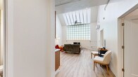 Located at 1707 Main St in La Crosse, Wisconsin, this one-bedroom, one-bathroom unit offers a thoughtfully designed single-floor layout. The living room is an immediate standout, boasting dramatically high ceilings with a skylight, a striking full-height glass block wall that floods the space with diffused natural light, and light hardwood-style flooring throughout. A wall-mounted mini-split unit provides climate control, complementing the clean, modern aesthetic.

The kitchen and living area share an open layout, with the kitchen featuring warm honey-toned cabinetry, a stainless steel sink, dishwasher, electric range, over-the-range microwave, and a full-size refrigerator — all finished in stainless steel. The light flooring continues seamlessly through this space, enhancing the airy feel.

The bedroom is a cozy, carpeted retreat with neutral walls and a window fitted with blinds that frame pleasant outdoor views of mature trees. A hallway connects the main living spaces to the bedroom and bathroom, providing a clear and functional flow.

The bathroom features a full tub-shower combination with a curtain rod, light hardwood-style flooring, and clean white fixtures, creating a simple and functional space. Overall, the unit offers a unique architectural character rarely found at this scale, anchored by its impressive vaulted living area.