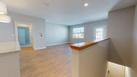 Located at 151 Oakland Rd in South Windsor, Connecticut, this single-floor residence offers a clean, modern design with a neutral color palette throughout. The open-concept living area is anchored by warm light hardwood flooring and large windows that invite natural light, with a glass-panel exterior door providing additional brightness and outdoor access. A wood-topped half-wall divides the living space from the kitchen area, adding architectural character while maintaining an open feel. The kitchen is well-appointed with rich dark cabinetry, granite countertops, stainless steel appliances including a range and built-in microwave, a subway tile backsplash, and a peninsula with pendant lighting — ideal for casual dining or meal prep. In-unit laundry is conveniently situated adjacent to the kitchen. The bedroom features plush wall-to-wall carpeting, multiple windows offering natural light and outdoor views, and a spacious walk-in closet outfitted with wire shelving and organizational racks. The full bathroom includes dark wood cabinetry with a white countertop vanity, a large mirror, combination tub/shower, and clean tile flooring. The space is finished with crisp white trim and baseboards throughout, presenting a well-maintained and move-in-ready environment.