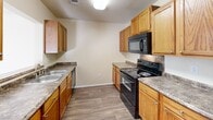 This single-story home offers a practical and comfortable layout with four bedrooms, three bathrooms, and a thoughtfully arranged floor plan. The kitchen is well-equipped, featuring warm honey-toned wood cabinetry, granite-look countertops, wood-look vinyl flooring, and a full suite of black appliances including a range, microwave, dishwasher, and refrigerator. A dedicated pantry closet provides additional storage directly off the kitchen. The bedrooms are carpeted and bathed in natural light through window blinds, with ceiling fans adding comfort throughout. The generously sized primary bedroom includes an en suite bathroom with dual sinks set in a wood-framed vanity with granite-look counters, a soaking tub, and a separate shower with sliding glass doors. A dedicated laundry room includes washer and dryer hookups and an overhead wire shelf for added utility. The hallways and bathrooms feature durable wood-look flooring that complements the warm neutral tones found throughout the home. Several rooms display crown molding and textured ceilings, adding subtle architectural detail. The layout flows efficiently, connecting the living areas to the bedroom wing through a central hallway, making the home feel organized and easy to navigate.
