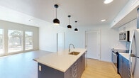 Located at 355 East 5th Avenue in Eugene, Oregon, this well-designed two-bedroom, two-bathroom residence offers a thoughtfully laid-out single-floor plan with a clean, contemporary aesthetic throughout. Light hardwood flooring flows through the main living areas, complementing the neutral white walls and modern finishes.

The open-concept kitchen and living area serves as the heart of the home, anchored by a striking blue kitchen island with light quartz countertops and an integrated sink. Pendant lighting hangs above the island, while stainless steel appliances—including a refrigerator, range, and microwave—are paired with two-tone cabinetry featuring dark lower and lighter upper units. A tiled backsplash adds texture to the cooking area.

Large, multi-panel windows in the living and bedroom areas flood the space with natural light and offer views of the surrounding Eugene neighborhood. A wall-mounted mini-split unit provides efficient climate control in the main living space.

The primary bedroom is a comfortable retreat with its own en-suite bathroom, which features a navy blue vanity with stone countertops, warm hardwood-style flooring, and direct access to a walk-in closet outfitted with wire shelving and hanging rods. The second bedroom features plush carpeting, while both bathrooms maintain a clean, modern design. Two closets throughout the residence provide ample storage.
