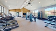Located at 5715 Glenwood Ave in Raleigh, NC, this single-floor fitness center is designed to deliver a comprehensive workout experience in a bright, modern setting. The space is defined by soaring vaulted ceilings with exposed white beams and a prominent ceiling fan that enhances airflow throughout the open floor plan. Warm wood-toned accent panels add a contemporary aesthetic contrast to the crisp white walls and speckled rubber flooring, which provides both durability and traction underfoot.

Large, floor-to-ceiling windows line multiple walls, flooding the interior with natural light while offering views of the surrounding community and outdoor pool area. This connection to the outdoors creates an energizing atmosphere well-suited for focused training. Full-length mirrors along one wall visually expand the space and assist with form during workouts.

The cardio section is well-appointed with multiple treadmills, stair climbers, ellipticals, stationary bikes, and rowing machines — all featuring personal display screens. The strength training area offers a robust selection of cable machines, multi-use weight stations, and a dedicated free weight section with a full dumbbell rack and adjustable benches. Recessed lighting and a wall-mounted flat-screen television round out the amenities, making this fitness center a fully equipped and inviting destination for residents.
