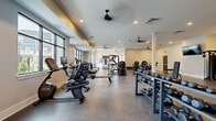 Located at 83 Terrace Greene Dr in Barboursville, VA, this single-floor fitness center offers an expansive, thoughtfully designed exercise facility. The space is divided into several distinct training zones, providing a comprehensive workout environment for users of all fitness levels.

The main floor features durable epoxy and rubberized flooring throughout, with smooth transitions between zones. Large black-framed windows line multiple walls, flooding the interior with natural light and offering views of the surrounding community. Ceiling fans are positioned throughout to maintain airflow and comfort.

The cardio zone is outfitted with treadmills, ellipticals, stationary bikes, and rowing machines, all arranged to face the windows. The strength training area includes extensive dumbbell racks, cable machines, a power rack, and weight benches, complemented by wall-mounted mirrors that enhance the sense of space. A dedicated functional training zone features artificial turf with agility lane markings, battle ropes, a sled track, suspension trainers, and a wall-mounted rig — all accessible through a full-width glass garage door that opens directly to the outdoors. Recessed lighting and mounted televisions complete the modern, clean aesthetic throughout this well-appointed fitness facility.