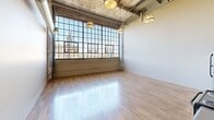 Located at 2320 E Superior Ave in Cleveland, OH, this striking three-bedroom, three-bathroom loft blends industrial heritage with modern functionality. The open living area commands attention with soaring ceilings, exposed concrete, visible ductwork, and expansive factory-style steel-framed windows that flood the space with natural light and offer sweeping urban views. Industrial pendant lighting complements the raw architectural character throughout.

The kitchen features rich, dark wood cabinetry paired with granite-look countertops, stainless steel appliances including a range and dishwasher, and a large window above — all set against the dramatic double-height backdrop. Warm hardwood-style flooring runs consistently throughout the living areas and bedrooms, creating a cohesive, inviting ambiance.

Each of the three bedrooms offers a neutral color palette, hardwood flooring, and dedicated closet space with built-in rods. The spacious primary bedroom provides a generous layout well-suited for comfortable living. The three bathrooms are cleanly finished with walk-in shower stalls featuring chrome fixtures, neutral tile flooring, and white vanities with large mirrors and overhead lighting. A connecting hallway ties the private quarters together efficiently, making this a well-organized and characterful urban residence.
