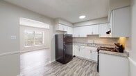 This single-floor residence in Lexington, Kentucky, offers a thoughtfully designed layout with a cohesive, neutral color palette and durable finishes throughout. The kitchen is a standout feature, equipped with crisp white shaker-style cabinetry extending to the upper walls for ample storage, granite-look countertops, black appliances including a refrigerator and range, and a stainless steel sink. Light gray wood-look vinyl plank flooring runs through the kitchen and main living areas, providing both style and easy maintenance. An adjoining dining area features chair-rail molding and an open connection to the kitchen, enhancing the sense of flow. The living area provides a welcoming entry point, with the same vinyl plank flooring and access to natural light through window treatments. The bedrooms offer plush wall-to-wall carpeting, ceiling-mounted light fixtures, and generous windows that invite natural light. One bedroom includes a built-in closet with shelving. The bathroom is finished with white tile surrounding a full tub-shower combination, wood-look flooring, and clean white fixtures. Textured ceilings are present throughout, adding a classic residential character to this practical and comfortable Lexington home.