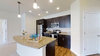 Located at 130 Ocean Aisle Circle in Salisbury, Maryland, this single-floor residence offers a thoughtfully designed living space with contemporary finishes throughout. The kitchen is a standout feature, showcasing rich, dark espresso-toned shaker-style cabinetry that extends to the ceiling, providing generous storage. Complementing the cabinetry are light-toned granite countertops with subtle veining, adding an elegant contrast to the overall design. The kitchen is fully equipped with stainless steel appliances, including a refrigerator, range with oven, and built-in microwave, making it both functional and stylish. A peninsula with a granite countertop extends into the living area, offering additional prep space and serving as a natural gathering point. Warm hardwood-style flooring runs throughout the kitchen, adding to the inviting ambiance. Recessed lighting and a pendant light above the peninsula ensure the space is well-lit and welcoming. The neutral white walls throughout provide a clean, versatile backdrop that enhances the brightness of the space. The open layout promotes a seamless flow, making this residence a comfortable and practical home.