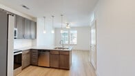 Located at 1200 Deer Moss Loop in Niceville, FL, this one-bedroom, one-bathroom unit offers a well-designed, single-floor layout that maximizes functionality and comfort. The open-concept kitchen serves as the heart of the space, boasting rich dark-wood cabinetry extending to the ceiling, granite countertops, a full suite of stainless steel appliances including a refrigerator, range, microwave, and dishwasher, and a peninsula island with an undermount sink. Three pendant lights hang above the island, providing both task lighting and visual warmth. Light wood-style flooring flows throughout the main living areas, complemented by a ceiling fan that enhances airflow. The living area receives natural light through a window overlooking the surrounding neighborhood. The bedroom is a comfortable retreat finished with soft carpeting, a ceiling fan, and two windows that bring in ample natural light. A dedicated walk-in closet with built-in shelving adds practical storage. The bathroom features a tiled tub-shower surround, a granite-topped vanity with dark cabinetry, and light wood-style flooring consistent with the rest of the unit. Clean white walls and neutral finishes throughout lend the space a bright, modern aesthetic.