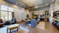 Located in Columbia, SC, the Edge Clubroom is a thoughtfully designed single-floor community space that blends comfort and sophistication across a generously sized open floor plan. The entrance welcomes visitors with soaring ceilings, bold "EDGE" lettering on a statement wall, and rich hardwood-style flooring that flows throughout the entire space.

The expansive living area serves as the heart of the clubroom, anchored by a floor-to-ceiling natural stone fireplace that commands immediate attention. Large multi-pane windows flood the room with abundant natural light, while a striking orb chandelier overhead adds an elegant focal point. Plush seating arrangements — featuring patterned armchairs, sofas, and a tufted ottoman — create inviting conversation areas well-suited for gatherings of any size.

Transitioning seamlessly into the kitchen and dining area, the space offers dark espresso cabinetry, granite countertops, a mosaic tile backsplash, and stainless steel appliances including a refrigerator, double wall oven, and microwave. A large central island with bar-height seating provides an ideal spot for casual dining or entertaining. A wall-mounted television and built-in counter nook add functional versatility to the kitchen zone, making this clubroom equally suited for both relaxed socializing and organized events.