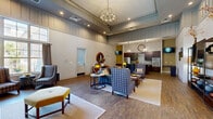 Located in Columbia, SC, the Edge Clubroom is a thoughtfully designed single-floor community space that blends comfort and sophistication across a generously sized open floor plan. The entrance welcomes visitors with soaring ceilings, bold "EDGE" lettering on a statement wall, and rich hardwood-style flooring that flows throughout the entire space.

The expansive living area serves as the heart of the clubroom, anchored by a floor-to-ceiling natural stone fireplace that commands immediate attention. Large multi-pane windows flood the room with abundant natural light, while a striking orb chandelier overhead adds an elegant focal point. Plush seating arrangements — featuring patterned armchairs, sofas, and a tufted ottoman — create inviting conversation areas well-suited for gatherings of any size.

Transitioning seamlessly into the kitchen and dining area, the space offers dark espresso cabinetry, granite countertops, a mosaic tile backsplash, and stainless steel appliances including a refrigerator, double wall oven, and microwave. A large central island with bar-height seating provides an ideal spot for casual dining or entertaining. A wall-mounted television and built-in counter nook add functional versatility to the kitchen zone, making this clubroom equally suited for both relaxed socializing and organized events.