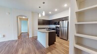 This single-floor residence offers a thoughtfully designed open-concept layout that seamlessly connects the kitchen and living areas. The kitchen serves as the centerpiece, showcasing rich dark espresso cabinetry, granite countertops, and a full suite of stainless steel appliances including a refrigerator, electric range, and over-the-range microwave. A large kitchen island with an integrated sink and matching granite surface provides both additional workspace and a natural gathering point. Elegant pendant lighting and recessed fixtures illuminate the space, while a white subway tile backsplash adds a clean, contemporary accent. Wood-look flooring flows throughout the main living areas, lending warmth and continuity to the open floor plan.

The bedroom is generously sized, featuring plush wall-to-wall carpeting, a ceiling fan, and a window fitted with blinds that allows for natural light. Adjacent to the bedroom is a dedicated walk-in closet with wire shelving, offering ample storage. The bathroom is clean and functional, outfitted with dark cabinetry topped with granite, a combination tub and shower, and wood-look flooring. A dedicated utility area houses the water heater and electrical panel. The arched doorways throughout add an architectural touch, contributing to the home's cohesive, modern aesthetic.