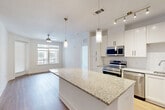 Located at 9113 Baltimore Ave in College Park, MD, this well-appointed 2-bedroom, 2-bathroom residence offers a thoughtfully designed single-floor layout. The heart of the home is an open-concept living, dining, and kitchen area bathed in natural light from large windows. The kitchen is a standout, featuring white shaker-style cabinetry, granite countertops, stainless steel appliances including a range and built-in microwave, a deep undermount sink, and a generous central island with pendant lighting overhead — ideal for both cooking and casual dining. Hardwood-style flooring flows throughout the main living areas, adding warmth and continuity to the space. The primary bedroom is spaciously proportioned, finished with plush carpeting and a ceiling fan, and connects directly to a luxurious en-suite bathroom. The primary bath showcases a double-sink granite vanity, light tile flooring, and an oversized glass-enclosed walk-in shower with elegant tile surround. A large walk-in closet with wire shelving provides ample storage. The second bedroom is equally comfortable, also featuring carpet and a ceiling fan. The second full bathroom offers a granite vanity and a tiled tub-shower combination. Additional highlights include four closets, a dedicated laundry area, and a utility room, rounding out this modern and functional residence.