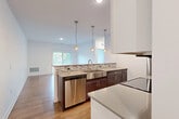 This well-appointed single-floor unit offers a thoughtfully designed open-concept layout that seamlessly connects the kitchen and living area. The kitchen serves as a standout feature, showcasing rich dark-stained cabinetry paired with light stone countertops, a mosaic tile backsplash, a stainless steel farmhouse sink, and a full suite of stainless steel appliances including a dishwasher, refrigerator, and range. Pendant lighting suspended above the kitchen island adds both function and style, while the space opens naturally into a bright living area with wood-look flooring and a sliding glass door that fills the room with natural light and outdoor views.

Two generously sized bedrooms are finished with plush patterned carpet and large windows that bring in ample daylight — one offering a view of surrounding greenery, the other overlooking the broader neighborhood. Both bathrooms are finished with light-toned tile flooring, dark-stained vanity cabinetry with white countertops, and full tub-shower combinations fitted with brushed nickel fixtures and built-in shelving. Clean white walls and consistent finishes throughout give the space a crisp, modern feel that is both inviting and functional.