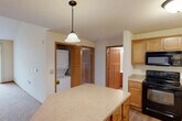 Located at 1918 Hawks Ridge Dr in Madison, WI, this two-story home offers a well-organized layout spread across two floors. The main level provides the larger share of living space and centers around a functional kitchen equipped with warm honey-toned cabinetry, a center island with a light countertop, black appliances including a range, microwave, dishwasher, and refrigerator, and durable wood-look flooring. Pendant lighting adds a polished touch overhead. A convenient in-unit stacked washer and dryer is tucked neatly into an alcove just off the kitchen. The main level also includes a full bathroom with a tub/shower combo, a single-sink vanity with warm wood cabinetry, and tile flooring. Three closets throughout the home provide ample storage, including a walk-in closet with built-in shelving and hanging rods. The upper floor is home to the generously sized primary bedroom, which features vaulted ceilings, plush carpeting, and a large sliding glass door with vertical blinds that fills the room with natural light. A second bedroom on the upper level also features carpet flooring and a ceiling fan with light fixture. A second full bathroom mirrors the clean, functional design of the first. The overall ambiance is bright, neutral, and move-in ready.