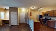 This single-floor residence offers a thoughtfully designed layout with functional living spaces and consistent finishes throughout. The kitchen is a standout feature, equipped with stainless steel appliances including a gas range, built-in microwave, refrigerator, and dishwasher. Rich medium-toned wood cabinetry pairs with granite-look countertops, and track lighting illuminates the galley-style workspace. A peninsula counter with bar-height seating separates the kitchen from the entryway, adding both utility and visual structure to the space. The open living area features dark hardwood-style flooring that extends throughout the home, warm beige-toned walls, and a ceiling fan with light fixture. Large windows and a glass door flood the room with natural light and provide access to the outdoors. A built-in desk nook adds a convenient workspace within the living area. The bedroom is a comfortable, well-proportioned room with a ceiling fan, a closet, and the same continuous hardwood-style flooring. The bathroom includes a single-sink vanity with granite-look countertop, rich wood cabinetry, a large mirror with overhead lighting, and a full tub-shower combo. Tile flooring completes the bathroom's clean and practical design.
