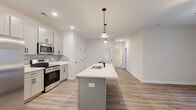 This well-designed single-story home in Clarksville, Tennessee offers 2 bedrooms and 3 bathrooms across a thoughtfully laid-out floor plan. The open-concept kitchen and living area serves as the heart of the home, featuring gray shaker-style cabinetry, a subway tile backsplash, stainless steel appliances, and a large center island with a built-in sink and pendant lighting overhead. Light wood-look LVP flooring runs throughout the main living areas, contributing to a clean, modern aesthetic. The living room is bright and airy, equipped with a ceiling fan and French doors that open to the outdoors, filling the space with natural light. The spacious primary bedroom is carpeted for comfort and includes a walk-in closet and ceiling fan. The second bedroom also features carpet and a standard closet. The three bathrooms are finished with gray vanity cabinetry, white countertops, and LVP flooring, with one bathroom offering a tub/shower combination. A dedicated laundry room accommodates full-size side-by-side washer and dryer units with overhead wire shelving for additional storage. The home's neutral color palette and consistent finishes throughout create a cohesive, move-in-ready living environment.