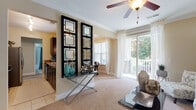This single-floor residence offers a thoughtfully designed layout that balances comfort and functionality throughout. The living area is bright and welcoming, featuring plush carpeting, crown molding, ceiling fans, and a sliding glass door that opens to a covered porch with stacked-stone columns—an ideal spot for outdoor relaxation. A decorative console with geometric mirror panels serves as a stylish divider between the living space and the adjacent kitchen.

The kitchen is outfitted with stainless steel appliances, including a range, over-the-range microwave, and refrigerator, complemented by granite countertops and dark cabinetry. The dining area, finished with carpet and large windows, connects seamlessly to the living room, creating an open and airy flow.

The bedrooms are carpeted and naturally lit, each equipped with a ceiling fan and ample space. One bedroom doubles as a flexible study or sitting area. Both bathrooms feature granite-topped vanities, dark-framed mirrors, and tiled tub-shower combinations. A dedicated in-unit laundry closet with wire shelving adds everyday convenience. Throughout, warm neutral tones and consistent finishes create a cohesive, polished ambiance.