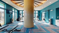 Located at 4011 Tryon Park Rd in Charlotte, NC, this well-appointed fitness center offers a comprehensive workout environment designed with both style and function in mind. The space is defined by bold teal accent walls, eye-catching herringbone-patterned flooring in teal and gray tones, and floor-to-ceiling windows that flood the interior with natural light and provide open views of the surrounding community.

A striking mosaic-tiled cylindrical column anchors the main cardio area, which is topped with a decorative coffered ceiling that adds architectural interest. This zone houses a full array of cardio machines, including treadmills, ellipticals, stair climbers, and a rowing machine, complemented by ceiling fans, wall-mounted televisions, and ample room to move.

The strength training area features a well-stocked dumbbell rack, weight benches, kettlebells, TRX suspension trainers, and a multi-functional fitness rig — all neatly organized along the teal walls. Stylish barn-style sliding doors connect the zones, adding a modern industrial touch.

A dedicated studio space offers hardwood flooring, large windows, BOSU balls, medicine balls, resistance bands, and a vibrant backlit mural wall, making it ideal for stretching, yoga, or functional training. A small refreshment station with a mini-fridge provides added convenience throughout the facility.